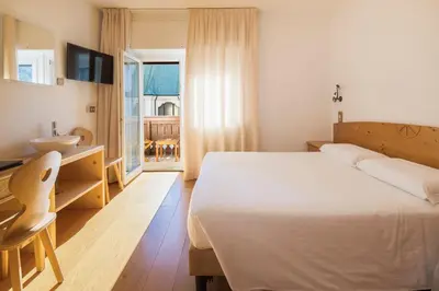 a bedroom with a white bed and a sink and a window at Hotel Montana in Cortina dʼAmpezzo