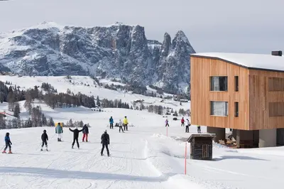 a group of people skiing in the snow next to a building at ICARO Hotel in Alpe di Siusi