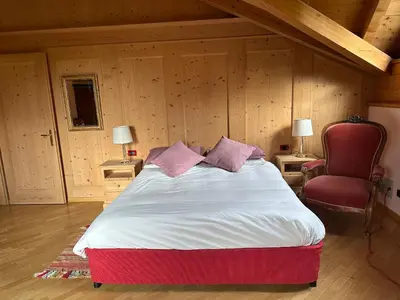 a bedroom with a large bed and a red chair at Casa del Cirmolo - apartments for rent in Cavalese