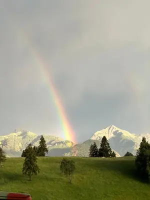 a rainbow in a field with mountains in the background at Casa del Cirmolo - apartments for rent in Cavalese