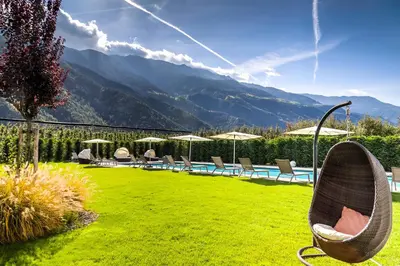 a garden with chairs and a pool and mountains at Residence & Sportlodges Claudia in Plaus