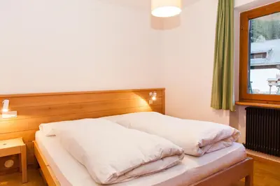 a bedroom with a bed with white sheets and a window at Appartamenti Chedul in Selva di Val Gardena