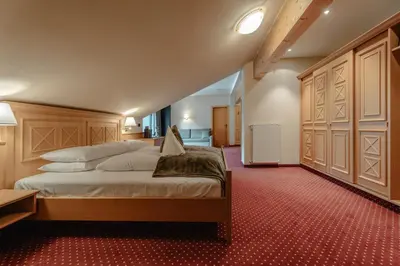 a bedroom with a large bed and a red carpet at Hotel Alpenrose in Carezza al Lago