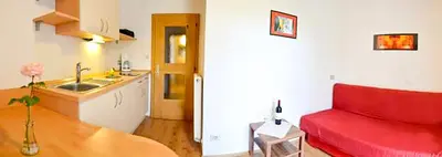 a living room with a red couch and a kitchen at Gästehaus Thaler in Caldaro