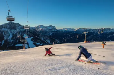 two people skiing down a snow covered slope with a ski lift at B&B Boutiquehotel Clara in Brunico