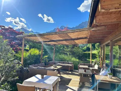 a person sitting on a patio under a wooden pergola at Hotel Garni Partaneshof in Merano