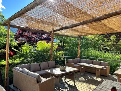 a pergola with couches and tables on a deck at Hotel Garni Partaneshof in Merano