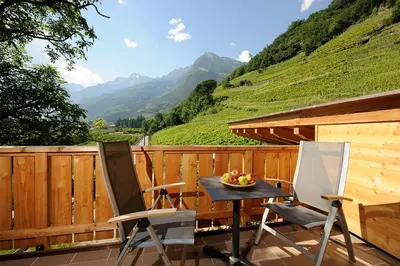 two chairs and a table on a deck with mountains at Hotel Garni Partaneshof in Merano