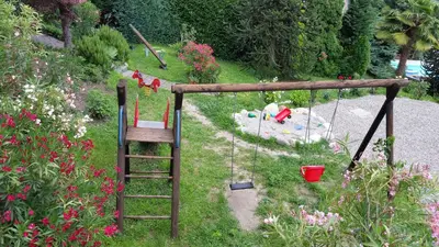 a playground with a ladder and a swing in a garden at Pension Weinberg in Rifiano