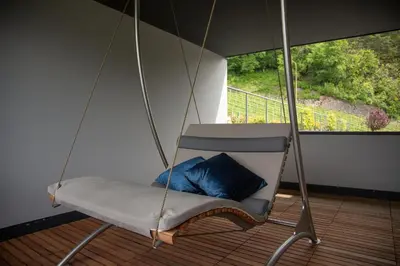 a swinging chair with a blue pillow on a porch at Romantik Chalet im Weingut Eichenstein in Merano
