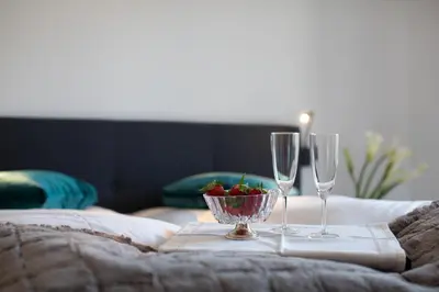 two wine glasses and a bowl of fruit on a bed at Appartments mir.es in Tirolo