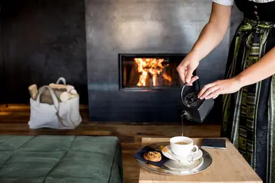 a woman pouring coffee into a cup in front of a fireplace at Romantik Hotel Turm in Fiè