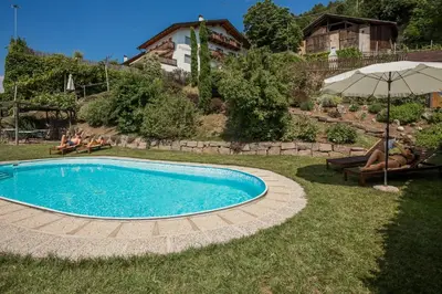 a swimming pool in a yard with people sitting under an umbrella at Engadiner Apartments & Wines in Montagna