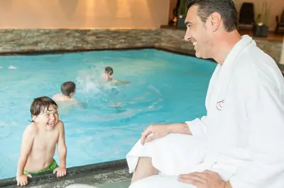 a man sitting next to a child in a swimming pool at Hotel Weihrerhof in Soprabolzano