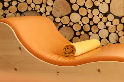 an orange chair in front of a wall of logs at Hotel Weihrerhof in Soprabolzano