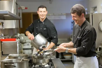 two men in a kitchen preparing food in a kitchen at Hotel Weihrerhof in Soprabolzano