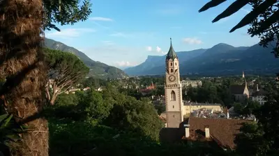 a building with a clock tower with mountains in the background at Apartment 39012 in Merano