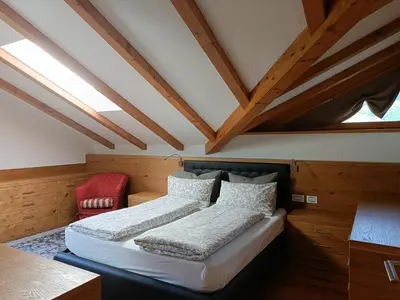 a bedroom with two beds and a red chair at Fiemme Deluxe Apartment in Castello di Fiemme