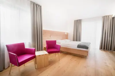 a bedroom with a bed and two purple chairs at Vegan Hotel La Vimea in Naturno