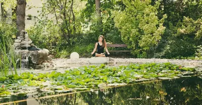 a woman sitting on a rock near a pond with water lilies at Vegan Hotel La Vimea in Naturno