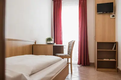 a bedroom with a bed and a chair and a window at Apparthotel Sellaronda in Arabba