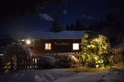 a log cabin with christmas lights in the snow at Brünnl's Försterhütte in Parcines