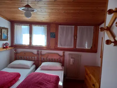 two beds in a room with wooden walls and windows at Casa Italo in Canazei