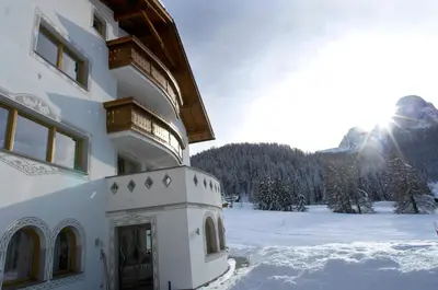 a building in the snow with the sun in the background at Residence Villa Funtanes in Selva di Val Gardena