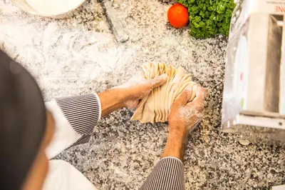 a person kneading pizza dough on a table at Hotel CampingPark Steiner in Laives
