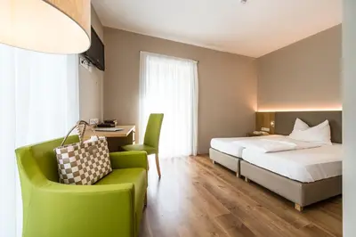 a hotel room with a bed and a green chair at Hotel CampingPark Steiner in Laives
