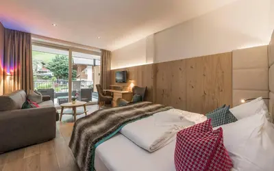 a hotel room with a bed and a living room at Stroblhof Active Family Spa Resort in San Leonardo in Passiria