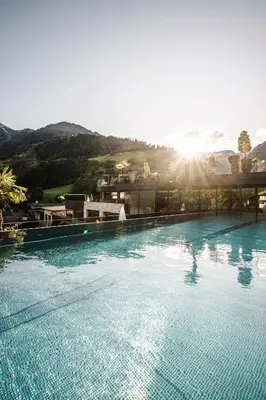 a large swimming pool with the sun in the background at Stroblhof Active Family Spa Resort in San Leonardo in Passiria
