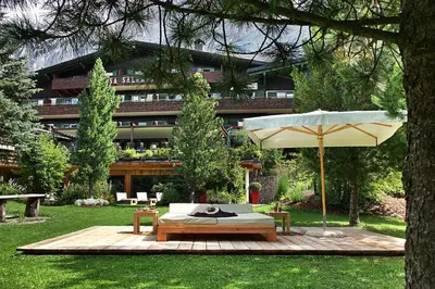 a patio with a table and an umbrella in a yard at Hotel Ciasa Salares in San Cassiano