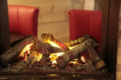 a fire in a fireplace with two red chairs at Wellness Hotel Lupo Bianco in Canazei