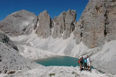 three people standing in front of a mountain lake at Wellness Hotel Lupo Bianco in Canazei