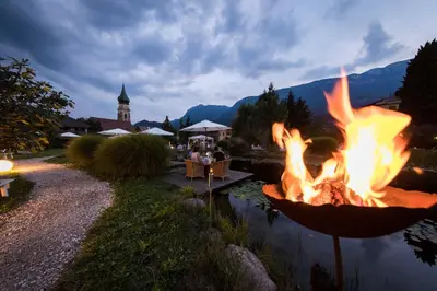 a fire pit next to a lake with people sitting at tables at Hotel Weingarten in Appiano sulla Strada del Vino
