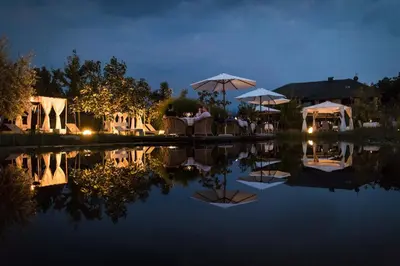 a restaurant with tables and umbrellas next to a pond at Hotel Weingarten in Appiano sulla Strada del Vino