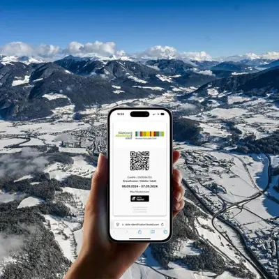 a person holding a cell phone in front of a mountain at HOTEL POST alpine cityflair in Brunico
