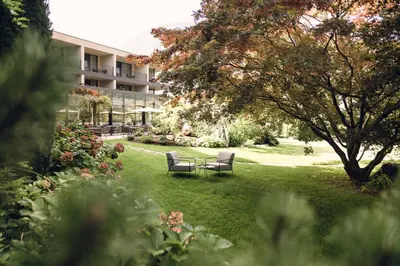 a park with two chairs and a table in the grass at Hotel Wiesenhof in Lagundo