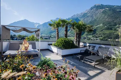 a woman sitting in a chair on a balcony with mountains at Hotel Wiesenhof in Lagundo
