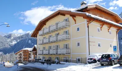 a large building in the snow with cars parked in front at Dolasilla Park Hotel in Vigo di Fassa
