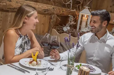 a man and woman sitting at a table with wine glasses at Miraval Hotel in Coredo
