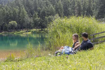 a man and woman sitting on a bench by a lake at Miraval Hotel in Coredo