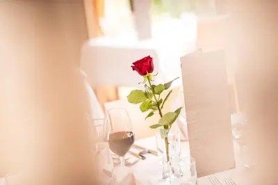 a rose in a vase on a table with wine glasses at Mounthotel Niggl in Nova Levante