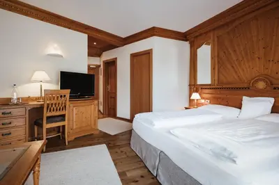 a bedroom with two beds and a desk and a television at Kristallhotel Corona-Krone in San Vigilio Di Marebbe