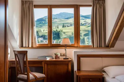 a bedroom with a bed and a desk with a window at Kristallhotel Corona-Krone in San Vigilio Di Marebbe