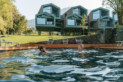 two people swimming in a pool in front of a house at Parc Hotel Florian in Siusi
