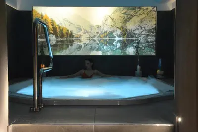 a woman in a hot tub with a large painting at Family Hotel Gran Baita in Pozza di Fassa