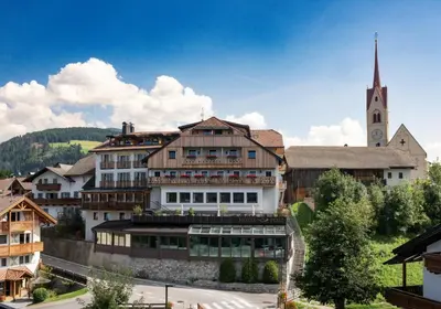 a large building with a church in the background at Hotel Post - Olang in Valdaora
