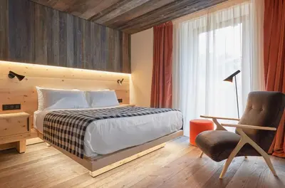 a bedroom with a bed and a chair and a window at HOTEL de LEN in Cortina dʼAmpezzo